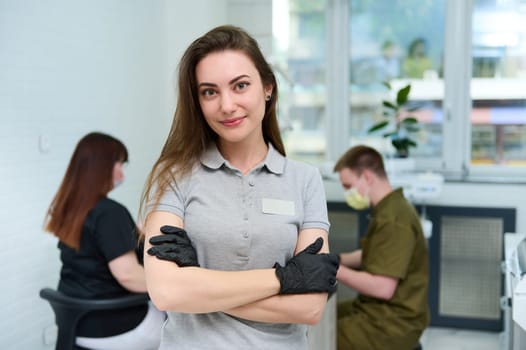 Caucasian successful committed young female dentist doctor looking at camera, standing with arms folded in dental office