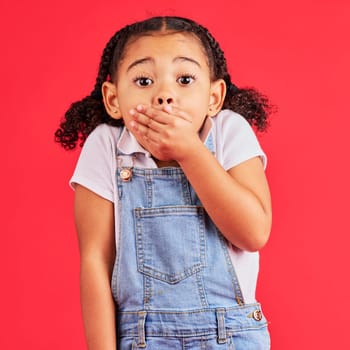 Shocked child, portrait and hand on mouth in secret, oops and mistake facial expression on isolated red background. Kid, little girl and surprised face in gossip, news or emoji at studio announcement.