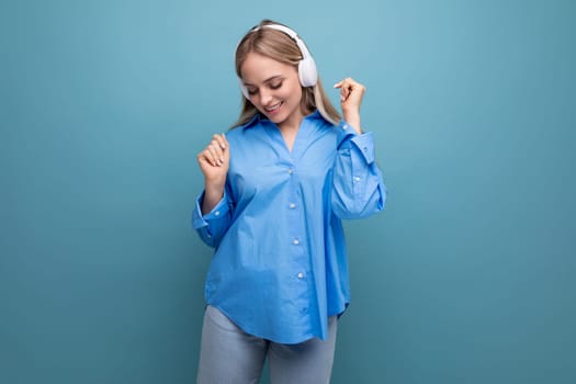 close-up of a charming girl with pleasure dancing in big headphones on a blue isolated background