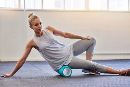 Fitness, physio and pilates, woman with roller on floor for leg tension and support in yoga workout at gym. Health, sports and massaging for physiotherapy massage, girl on ground foam rolling muscle.
