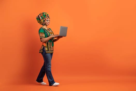 Smiling african woman freelancer with laptop on orange background