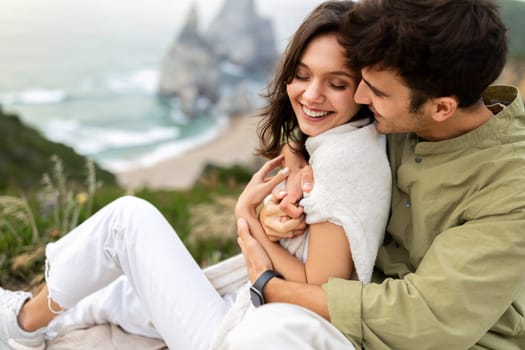 Romantic seaside embrace. Happy young couple hugging and smiling, having date with breathtaking view at coastline