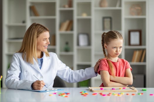 Behavior Therapy For Kids. Smiling Psychotherapist Woman Working With Grumpy Little Girl
