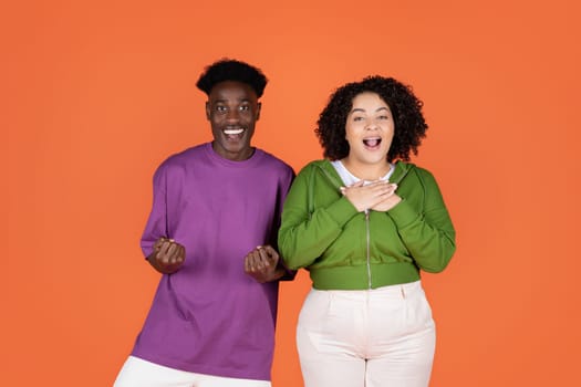 Amazed excited multicultural couple gesturing on orange background