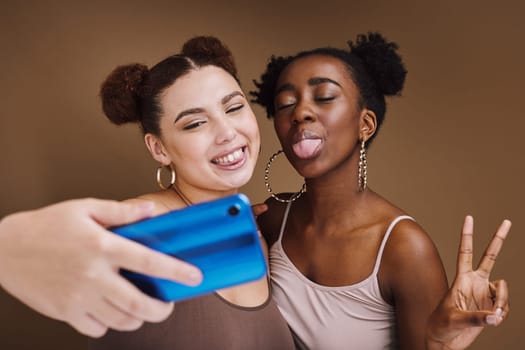 Fashion, selfie and friends with phone with peace sign on brown background for wellness, cosmetics and makeup. Jewellery, happy and girls smile on smartphone for social media, picture and online post