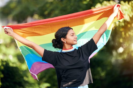 Rainbow, flag and human rights with an indian woman in celebration of lgbt gay pride alone outdoor. Freedom, equality and lgbtq with a happy female outside celebrating her equality or inclusion
