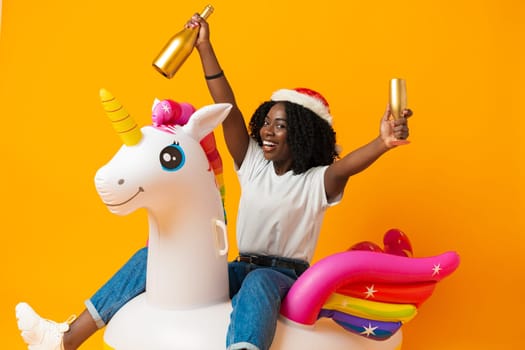 African woman sitting on rainbow unicorn float wearing santa claus hat in studio