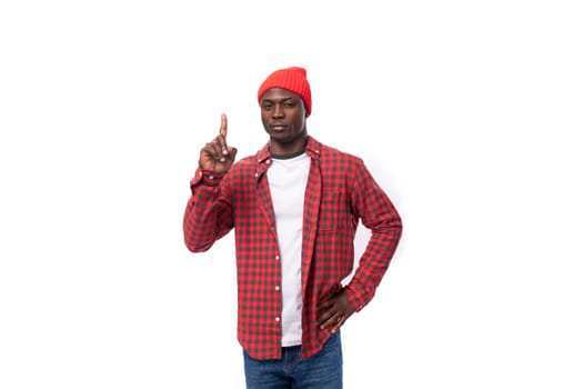 smart confident young american man in red cap and plaid shirt uses hands to gesticulate in advertising on white background with copy space