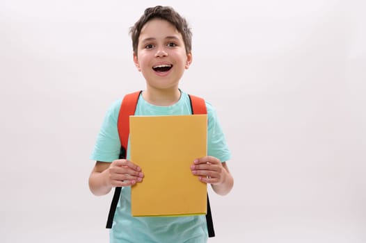 Emotional happy teenage school boy holding textbooks, smiling looking at camera, standing over white isolated background