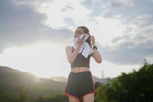 Wiping sweat after run Young athletic woman exercising in the city park outdoors