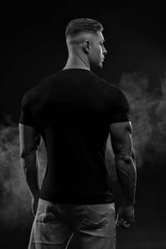 Athletic sexy man in black t-shirt and jeans posing in studio back view
