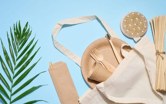 White cotton bag, wooden forks, plates and cups on a blue background. Waste recycling concept, zero waste