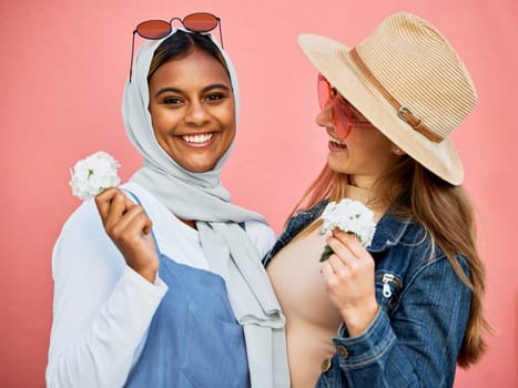 Happy, portrait and lesbian couple with flowers isolated on a pink background in a studio. Smile, looking and Muslim girl with a flower, woman and happiness about plants for romance on a backdrop.