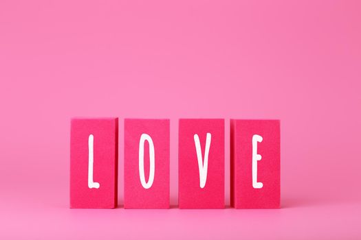 Word love written on pink toy blocks against pink background with copy space