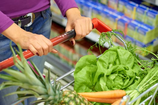 Woman, shopping cart and customer with grocery, vegetables or fruit and healthy food for diet, nutrition and supermarket. Market, store or person to shop groceries and carrot, lettuce and pineapple.