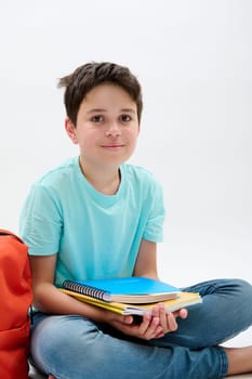 Vertical studio portrait of a handsome happy positive school kid boy holding school supplies, smiling looking at camera