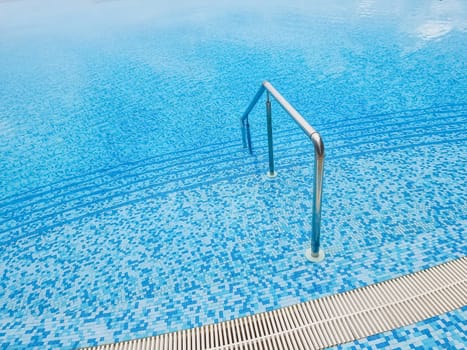 Beautiful pool with a Metal Handrails Descent and blue water at sunset. Swimming and summer rest concept.pool with a metal handrail. Safety for water sports
