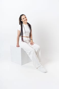 Fashionable young beautiful woman . Slim girl with dreadlocks in an active pose in a white pants and top . Fashion, clothing and style.