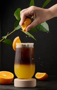 Iced coffee with orange juice in a transparent glass, a woman's hand squeezes an orange slice into a bubble drink