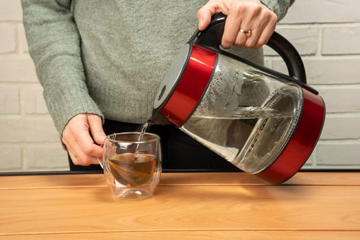 woman pouring hot water from a kettle into a clear glass mug