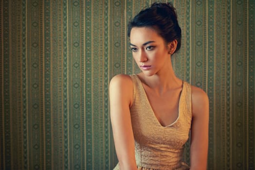 Shes got a sophisticated style. a beautiful and elegant young woman posing in a green wallpapered room.