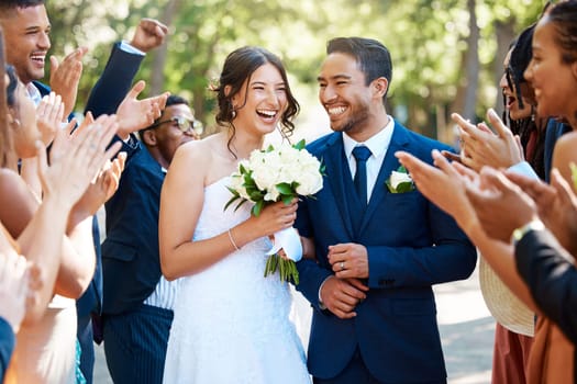 Couple, wedding and guests clapping hands in celebration of love, romance and union. Happy, smile and young bride with a bouquet and groom walking by crowd cheering for marriage at an outdoor event