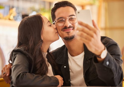 Selfie, love and kiss with a couple on a date at a restaurant together in celebration of their anniversary. Photograph, dating or kissing with a man and woman bonding or celebrating in a coffee shop.