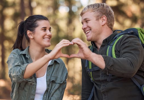 Love, couple and heart hands while hiking in nature for affection or support. Emoji, hand gesture and romance or intimacy shape with happy man and woman on adventure or trekking outdoors in forest