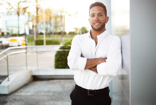 Successful male entrepreneur. Outdoors portrait of european businessman posing near office building with folded arms
