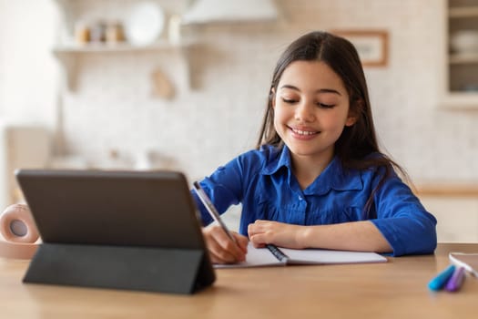 School kid girl learning at tablet taking notes at home