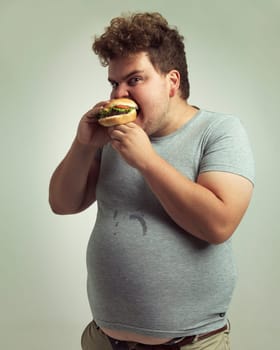 Dont come near my burger. Studio shot of an overweight man biting into a burger.