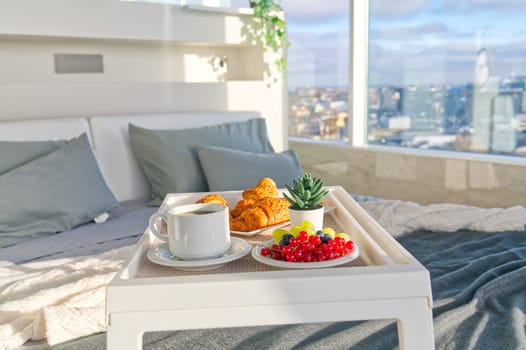 White Tray with tasty breakfast on bed in light bedroom with big windows in skyscraper. lifestyle
