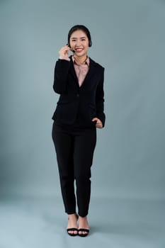 Attractive full body asian female call center operator with happy face advertises job opportunity on empty space, wearing formal suit and headset on customizable isolated background. Enthusiastic