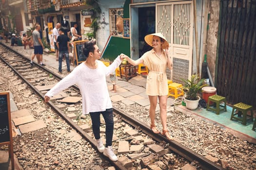 First rule of travel Find true love. a young couple walking on the train tracks through the streets of Vietnam