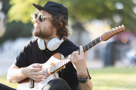 A man hipster wearing sunglasses playing guitar in the park