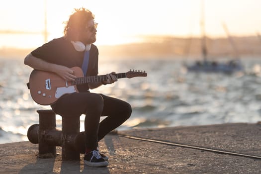 A man sits at the quay and playing guitar at early sunset