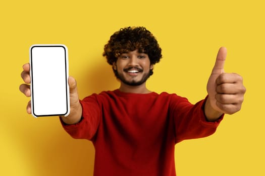 Smiling hindu guy showing cell phone and thumb up