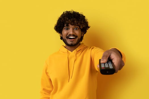 Amazed happy young eastern guy holding TV remote control