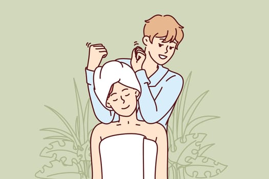 Woman visits massage therapist in SPA salon and sits in towel enjoying relaxing treatments. Man works in SPA center giving shoulder and neck massage to visitor in need of manual procedures