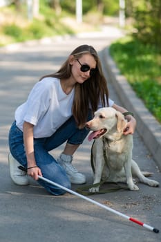 Blind young woman cuddling with guide dog on a walk outdoors.