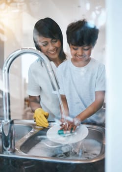 Woman, boy child and dishes at kitchen sink for learning, cleaning and hygiene with care in family house. Mother, boy and washing play with soap, water and teaching for skills, chore or stop bacteria