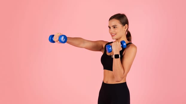 Sporty woman doing exercises with dumbbells on pink studio background