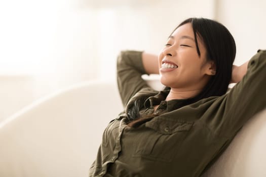 Relaxed smiling asian lady chilling on couch, copy space