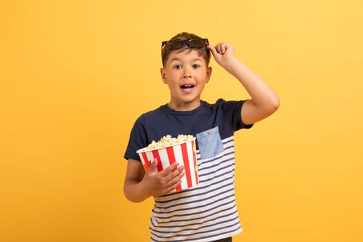 Amazed kid boy with popcorn in 3d glasses on yellow