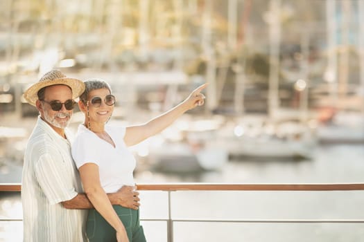 Joyful Mature Couple Embracing Pointing Finger At Sailboats At Marina
