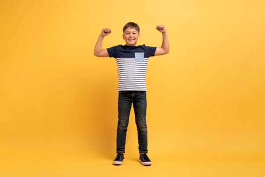 Strong cute kid boy showing muscles, yellow background