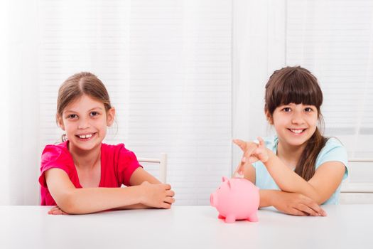 Girls putting coin into piggy bank