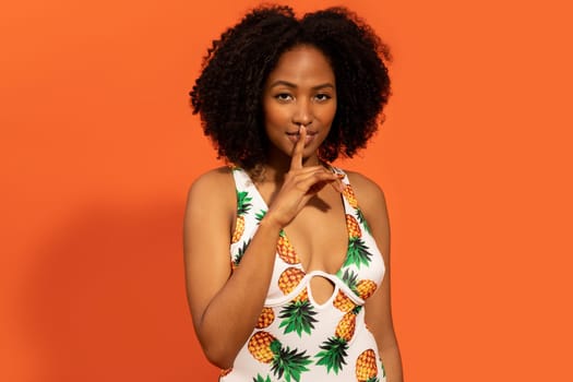 Playful attractive african woman in swimwear holding finger on lips