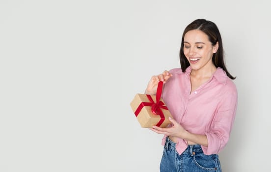 Thrilled woman in pink opening gift box and smiling
