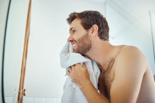 Man, cleaning face and towel in mirror with smile, self care and hygiene to start morning in home bathroom. Young guy, person and cloth for beauty, facial cosmetics and wellness for beard in house